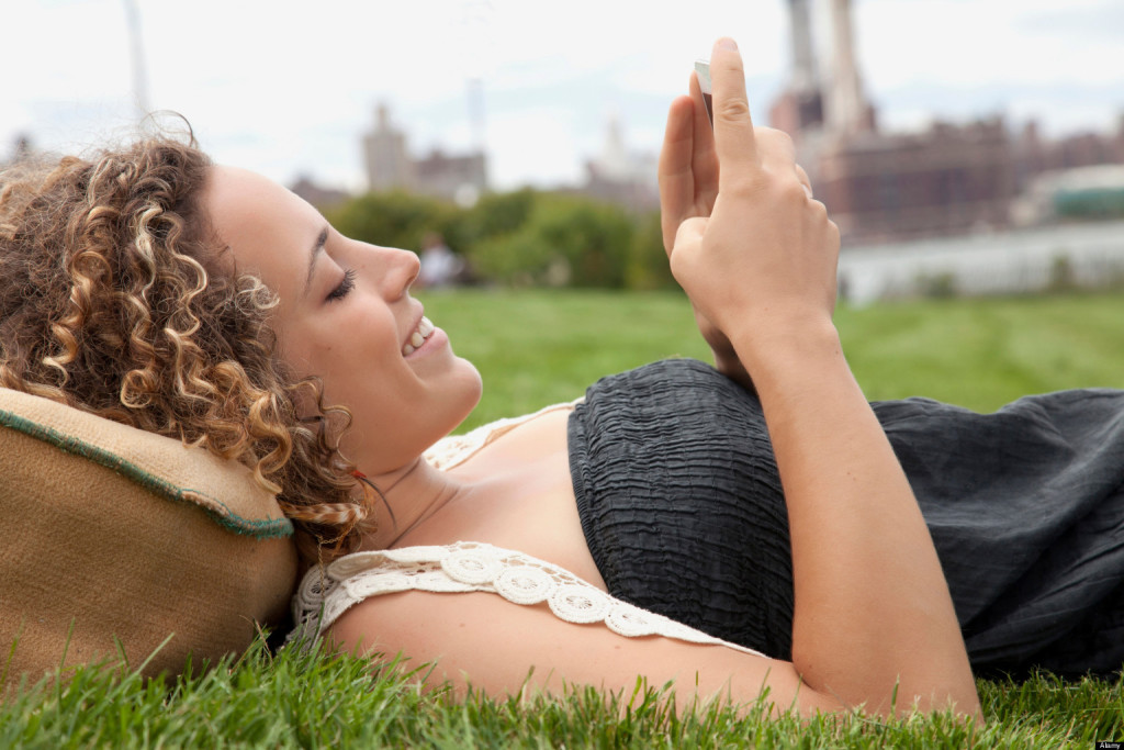 CX12Y1 Young woman lying on grass and looking at smartphone